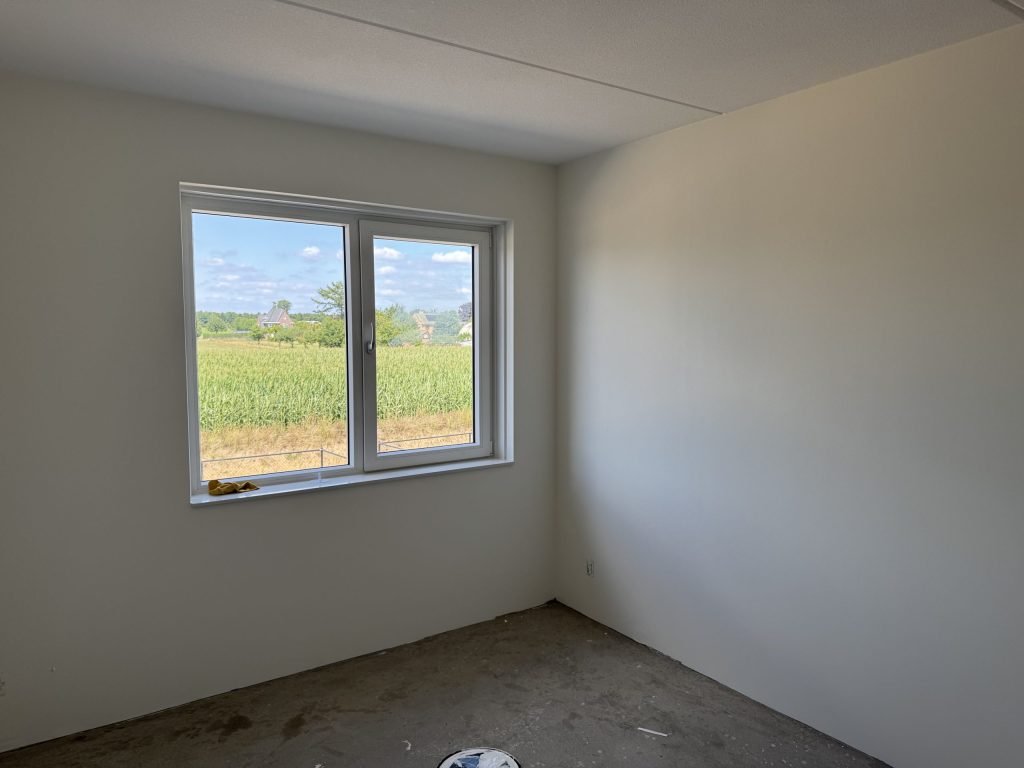 Lege slaapkamer met lichte vlakke wanden en een breed raam met uitzicht op het groen
