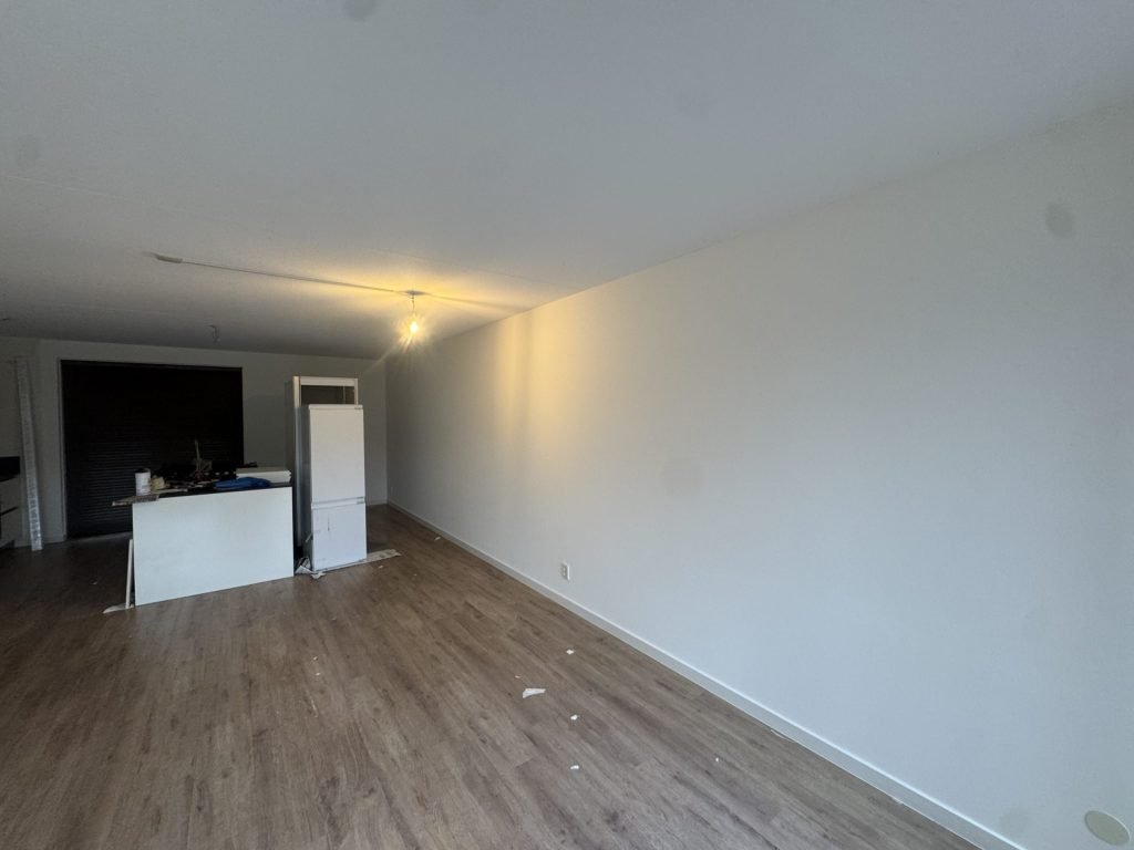 Lege woonkamer van een appartement met houten vloer, open keuken en een strakke witte wand